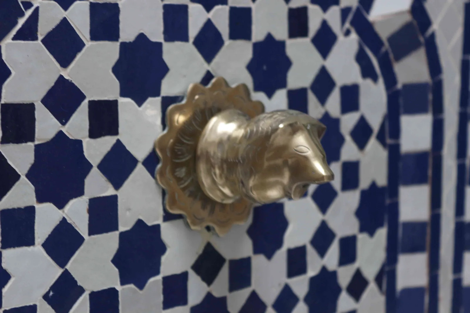 A brass door knocker on blue zellige tile
